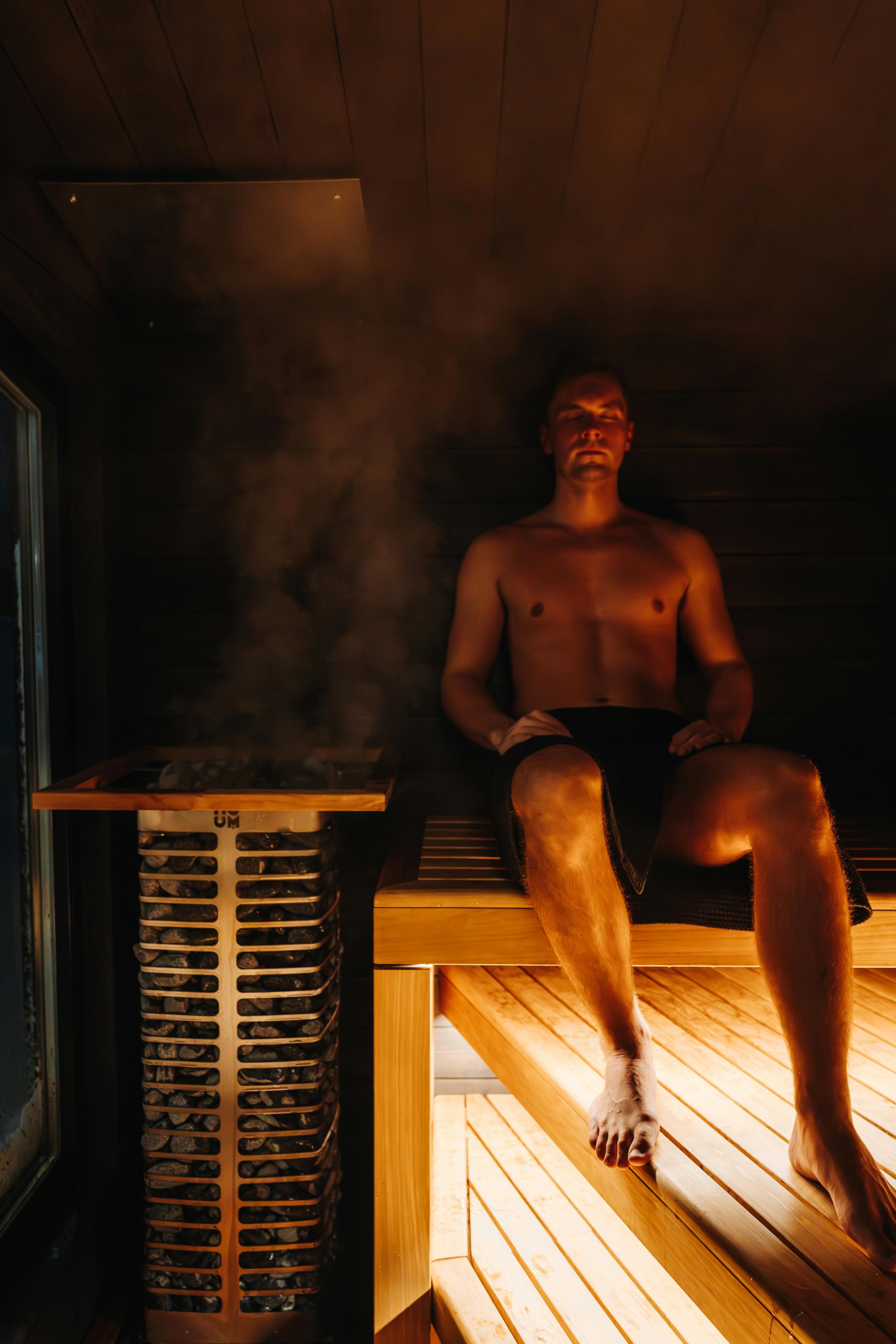 Un homme est assis dans un sauna, près d'un poêle fumant.