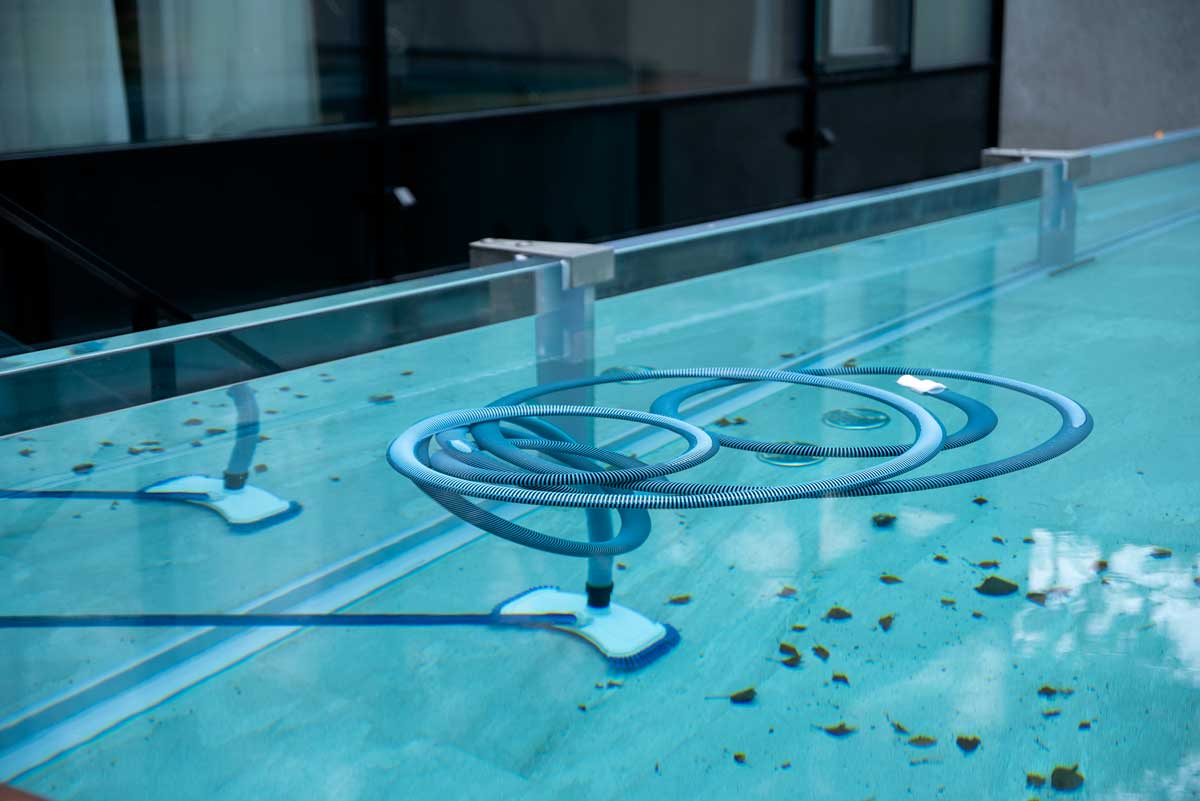 Balai de nettoyage immergé dans l'eau de la piscine extérieure, pour nettoyer le fond et les parois, piscine pleine de feuilles et autres signes de négligence - saleté