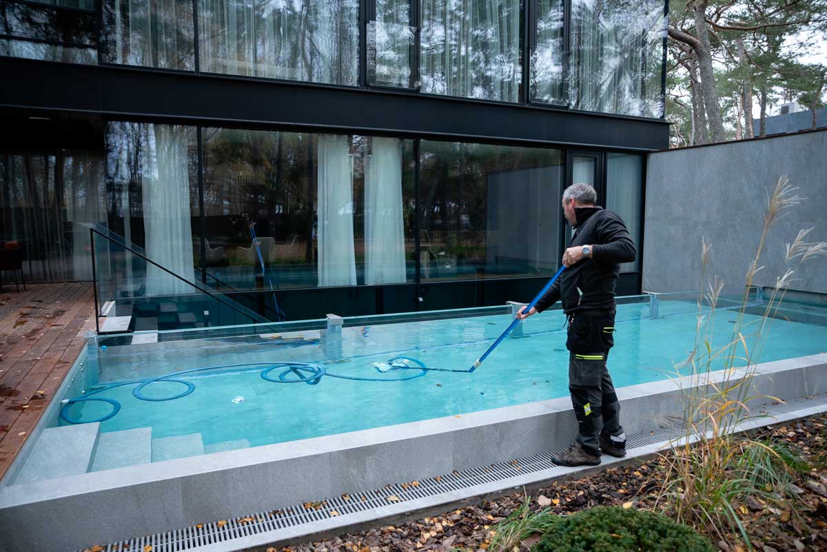 Piscine extérieure à l'eau trouble et sale, avec des taches brunes et des saletés visibles à la surface ; une personne se tient au bord de la piscine.