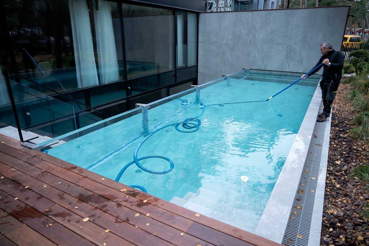 Une piscine à l'eau vert clair et trouble, la surface recouverte d'une couche d'algues, situation capturée alors qu'une personne nettoie la piscine.