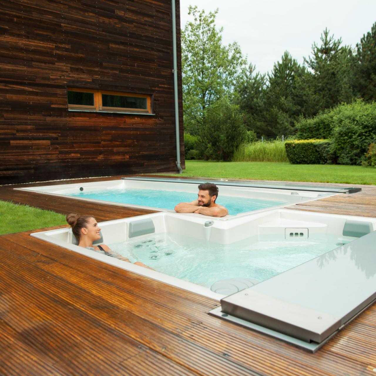 Un couple se détend dans les piscines extérieures USSPA (spa et spa de nage) installées sur une terrasse en bois.