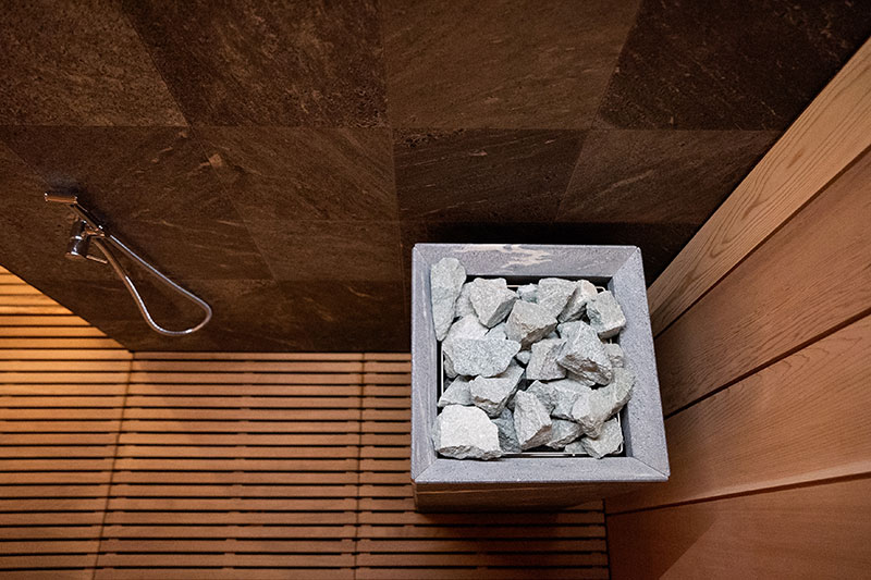 Vue de dessus d'un poêle de sauna avec des pierres gris clair, des grilles en bois et des carreaux muraux foncés.