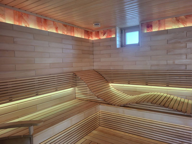 Sauna en bois clair avec banc ondulé et éclairage LED.