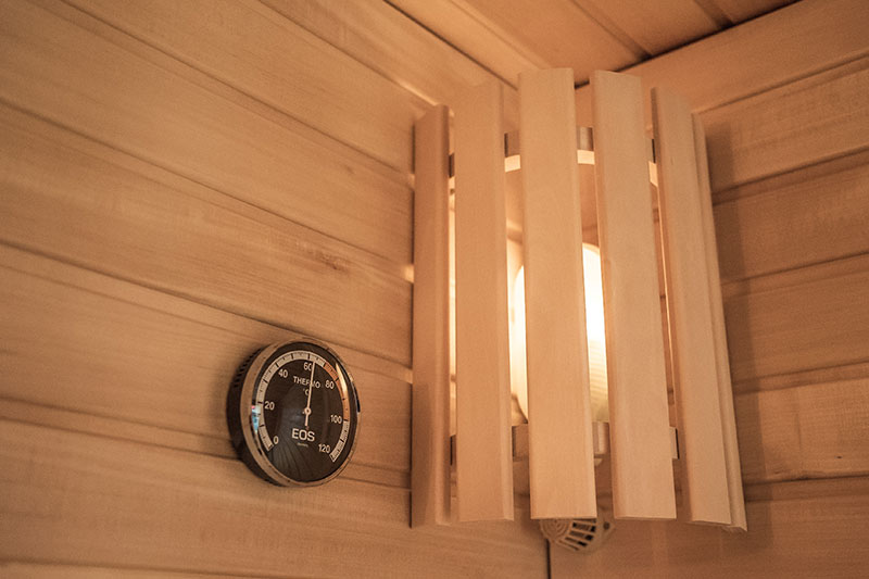Thermomètre de sauna EOS et abat-jour en bois dans le coin.